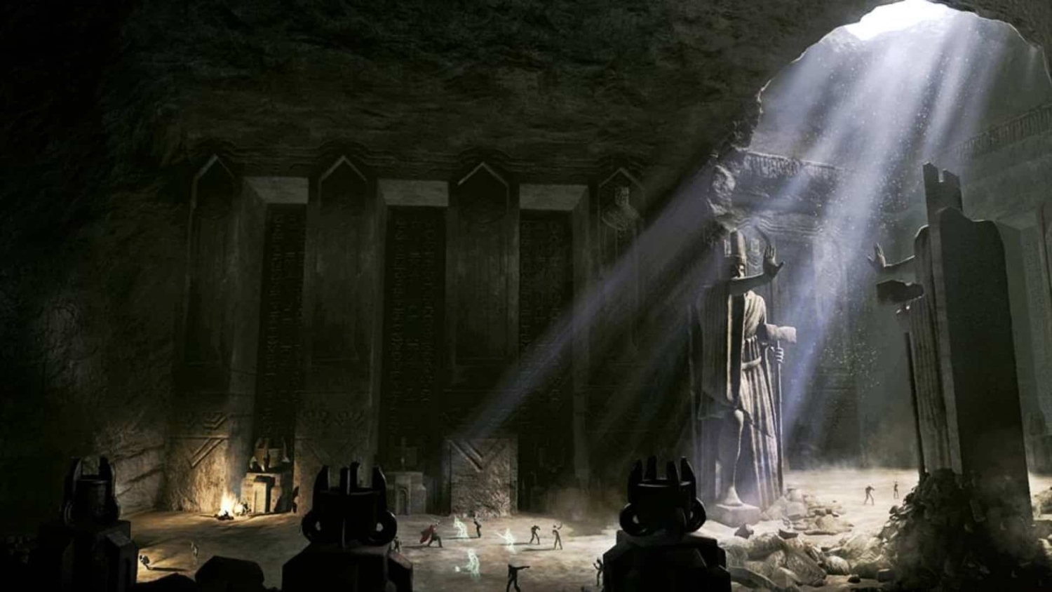 Light beams shine through an opening illuminating a large stone statue inside an ancient underground chamber with scattered figures