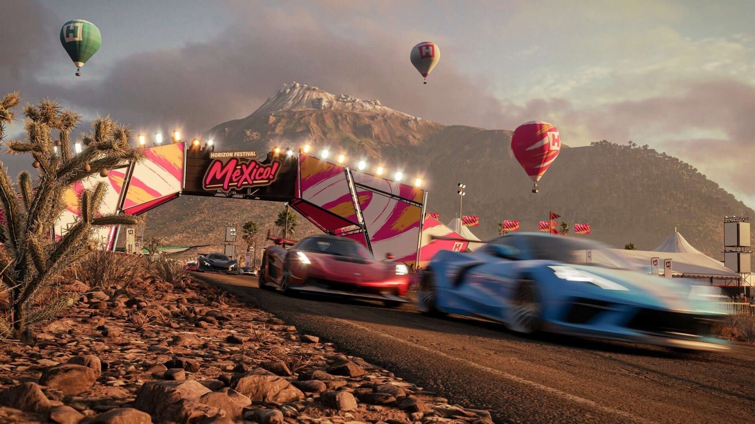 Sports cars speeding past Horizon Festival Mexico entrance with hot air balloons and mountainous landscape