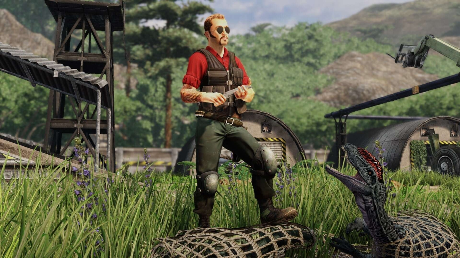 Man in tactical gear and sunglasses stands in a grassy field near a small dinosaur with open mouth