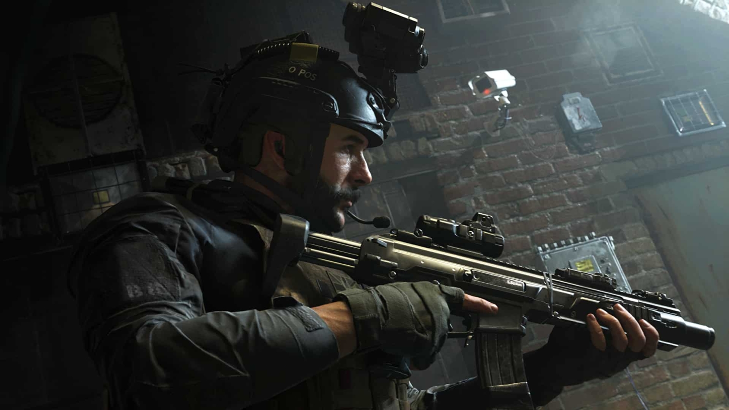 Soldier in tactical gear aiming rifle inside a dimly lit urban building with brick walls and surveillance cameras