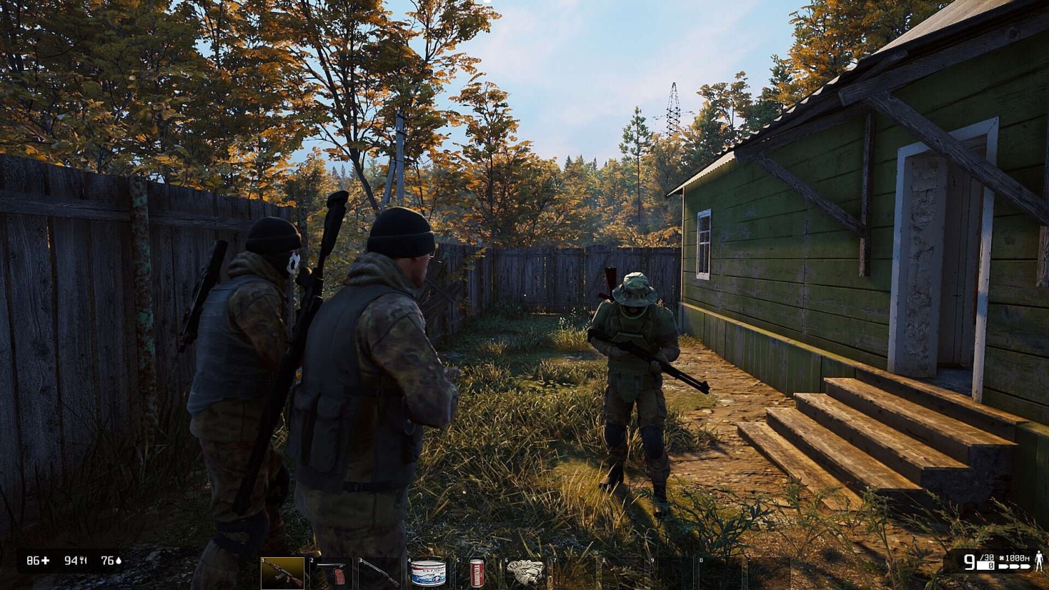 Three armed soldiers in camouflage gear standing close to a green wooden house in an autumn forest setting