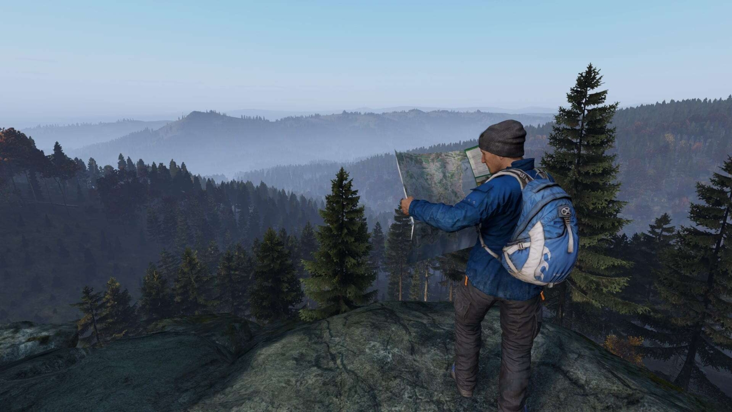 Man wearing blue jacket and beanie reading a map on rocky hill with forest hills in misty distance
