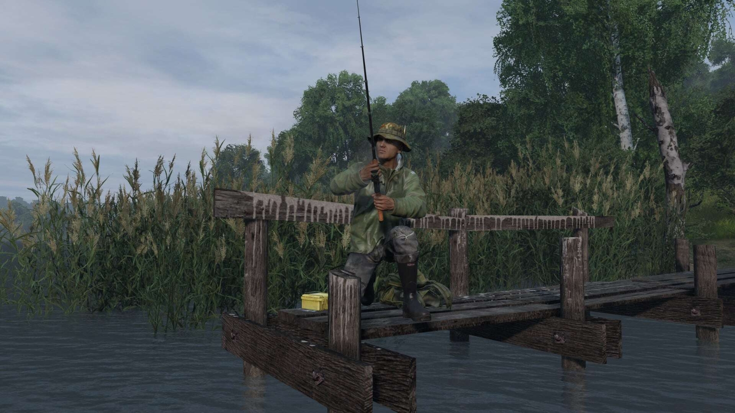 Man kneeling on wooden dock holding a fishing rod surrounded by reeds and trees under a cloudy sky
