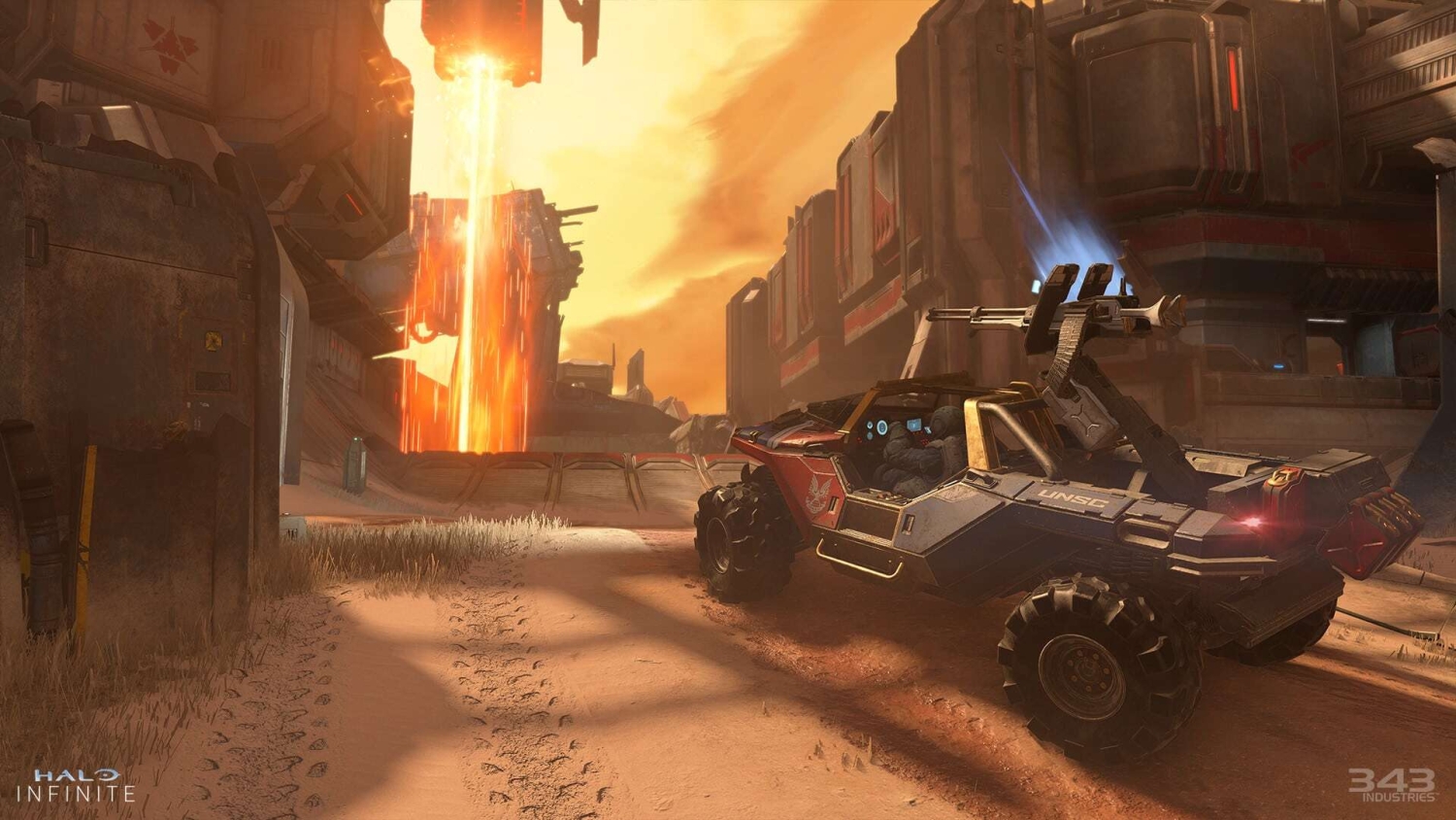 Armoured military all-terrain vehicle driving on dusty terrain near sci-fi industrial structures at sunset