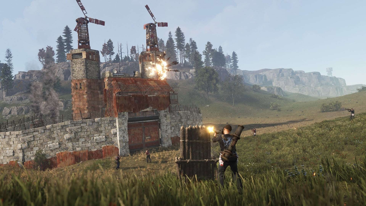 Players armed with guns and rocket launcher attack a large fortified base with stone walls and windmills in grassy wilderness
