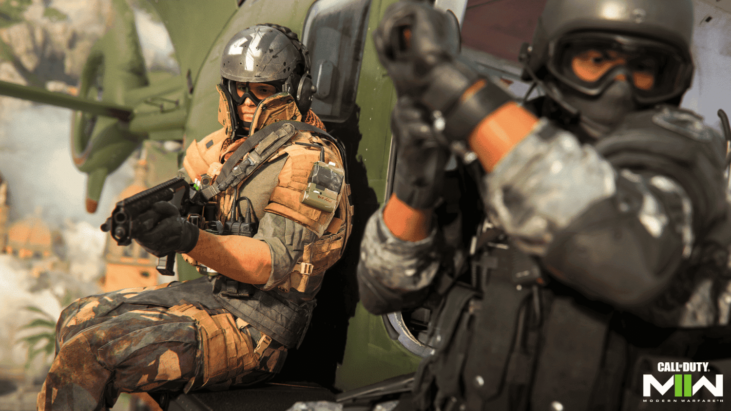 Two soldiers in tactical gear with helmets and goggles armed and ready beside a green military helicopter