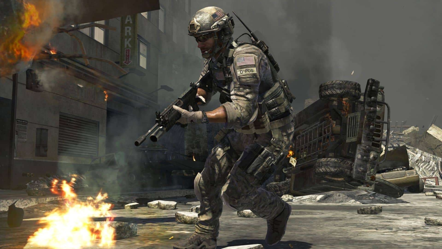 Soldier in modern combat gear advancing cautiously through a burning city street with overturned vehicles and smoke