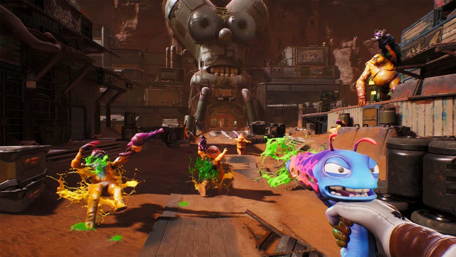 First-person view of a player firing a colourful gun at orange alien creatures splattered with green slime in a dusty desert town