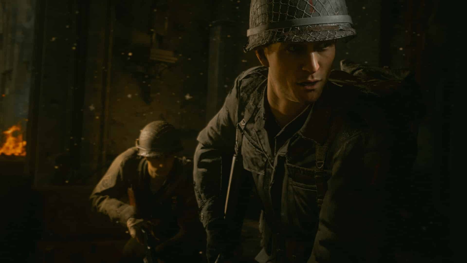 Two soldiers in World War II uniform inside a dimly lit building with fire glowing outside