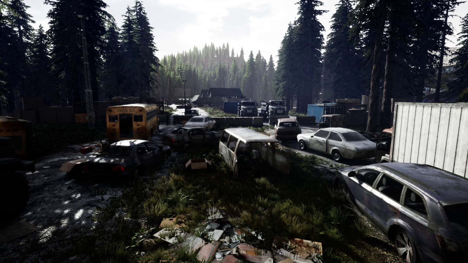 Abandoned cars and a derelict school bus scattered in a forest clearing with tall trees and a cloudy sky