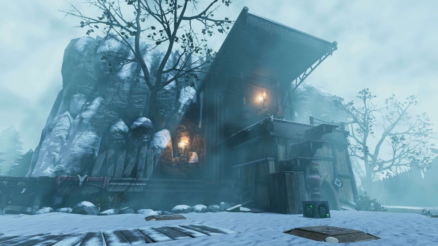 Wooden building on snowy ground with glowing lanterns under foggy sky and rocky background