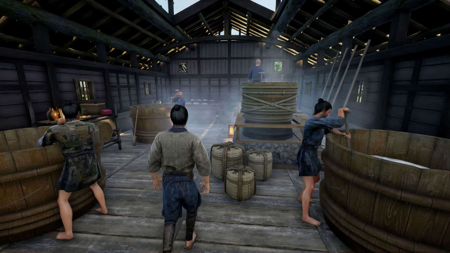 Workers in traditional attire stirring large wooden vats inside a smoky wooden building with sloped roof beams