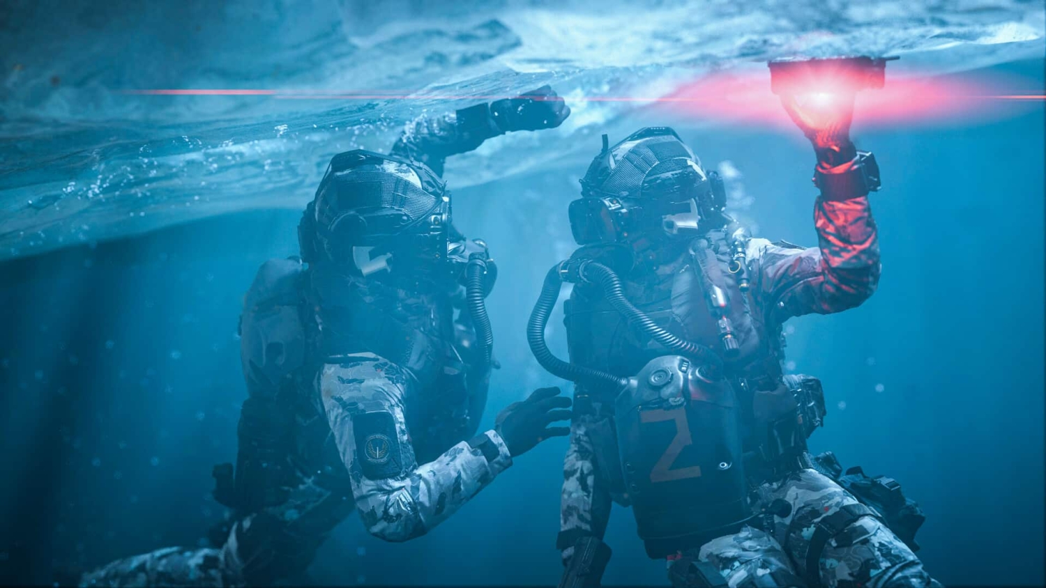 Two divers in tactical gear underwater inspecting an ice ceiling with a red light