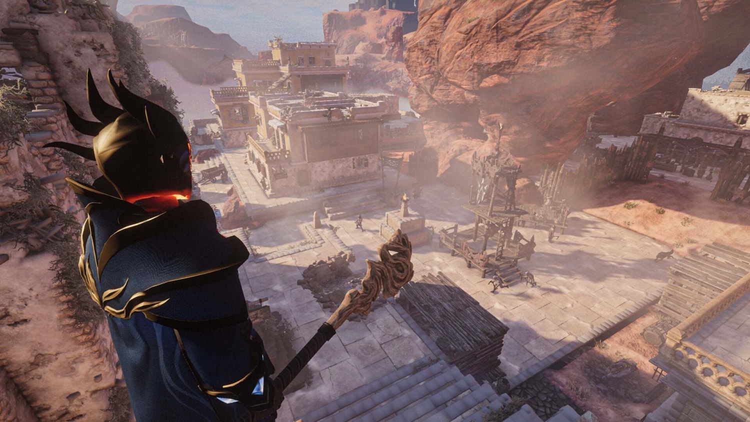 Dark-armoured figure holding ornate wooden staff looks over a desert village with stone buildings and rocky cliffs