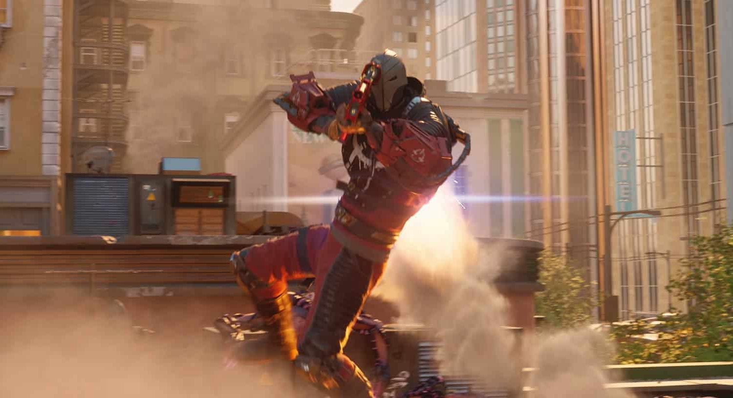 Armoured character in red and black suit firing weapon amid urban destruction with dust and debris around