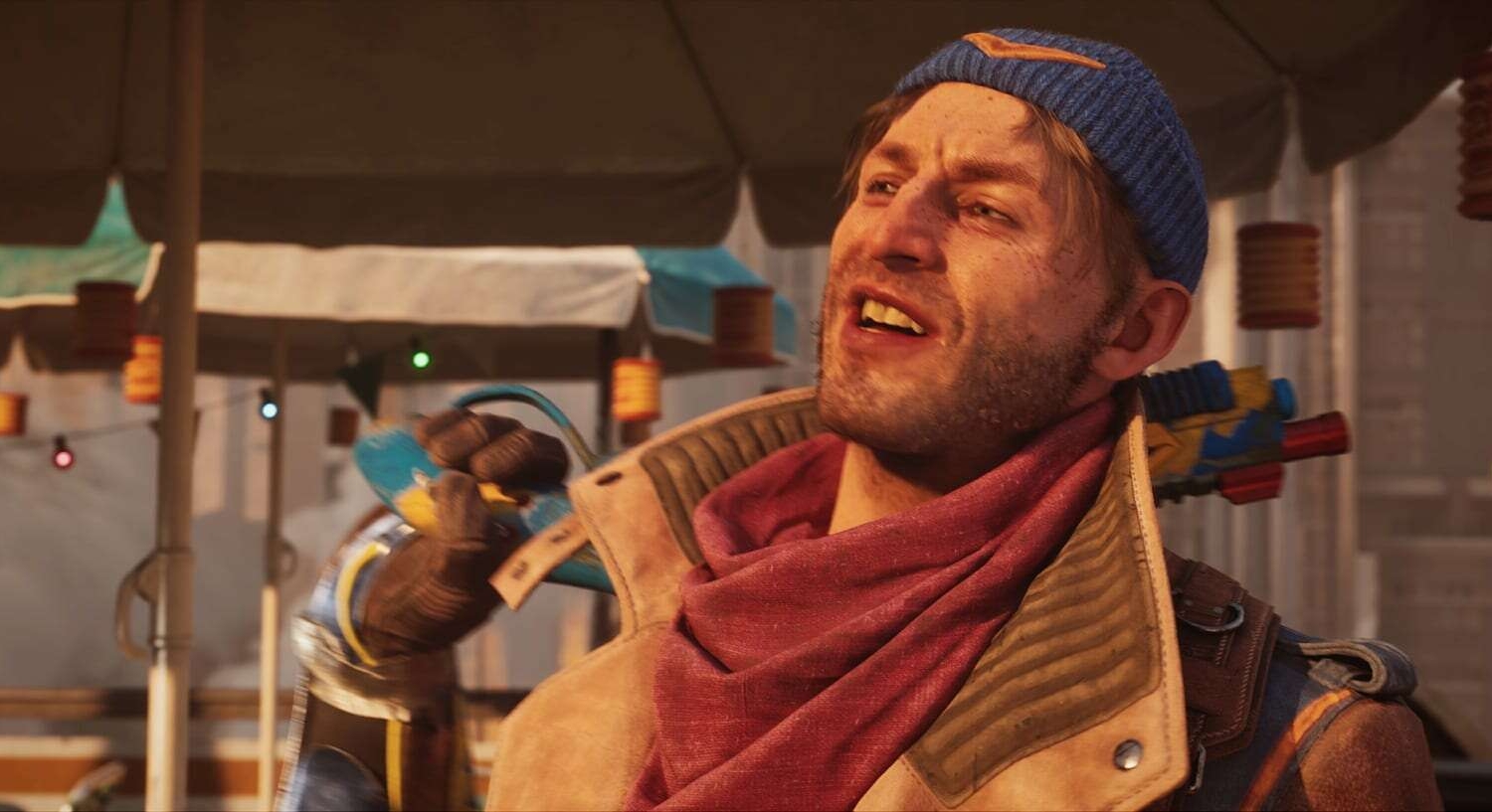 Man wearing a blue beanie and red scarf smiles while holding a colourful weapon over his shoulder inside a market tent