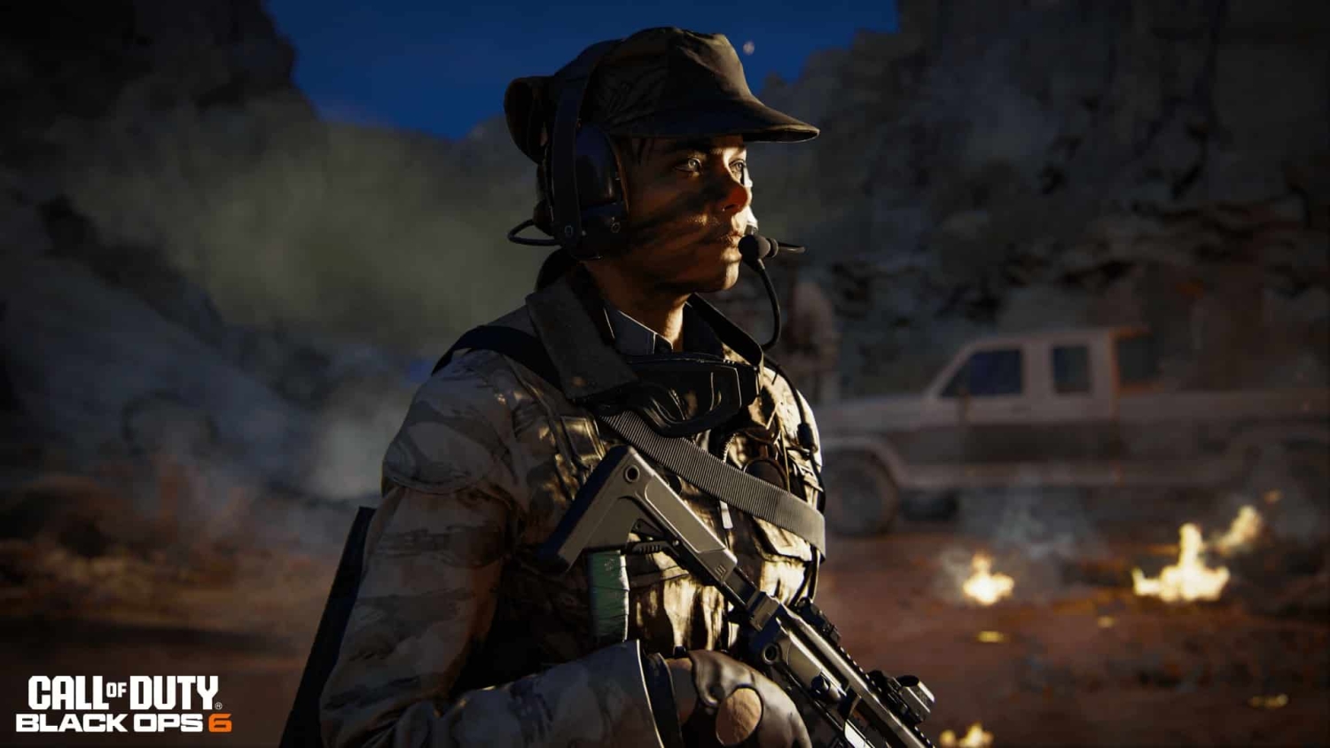 Soldier wearing headset and camouflage gear holding rifle in desert environment at dusk with smoke and fire