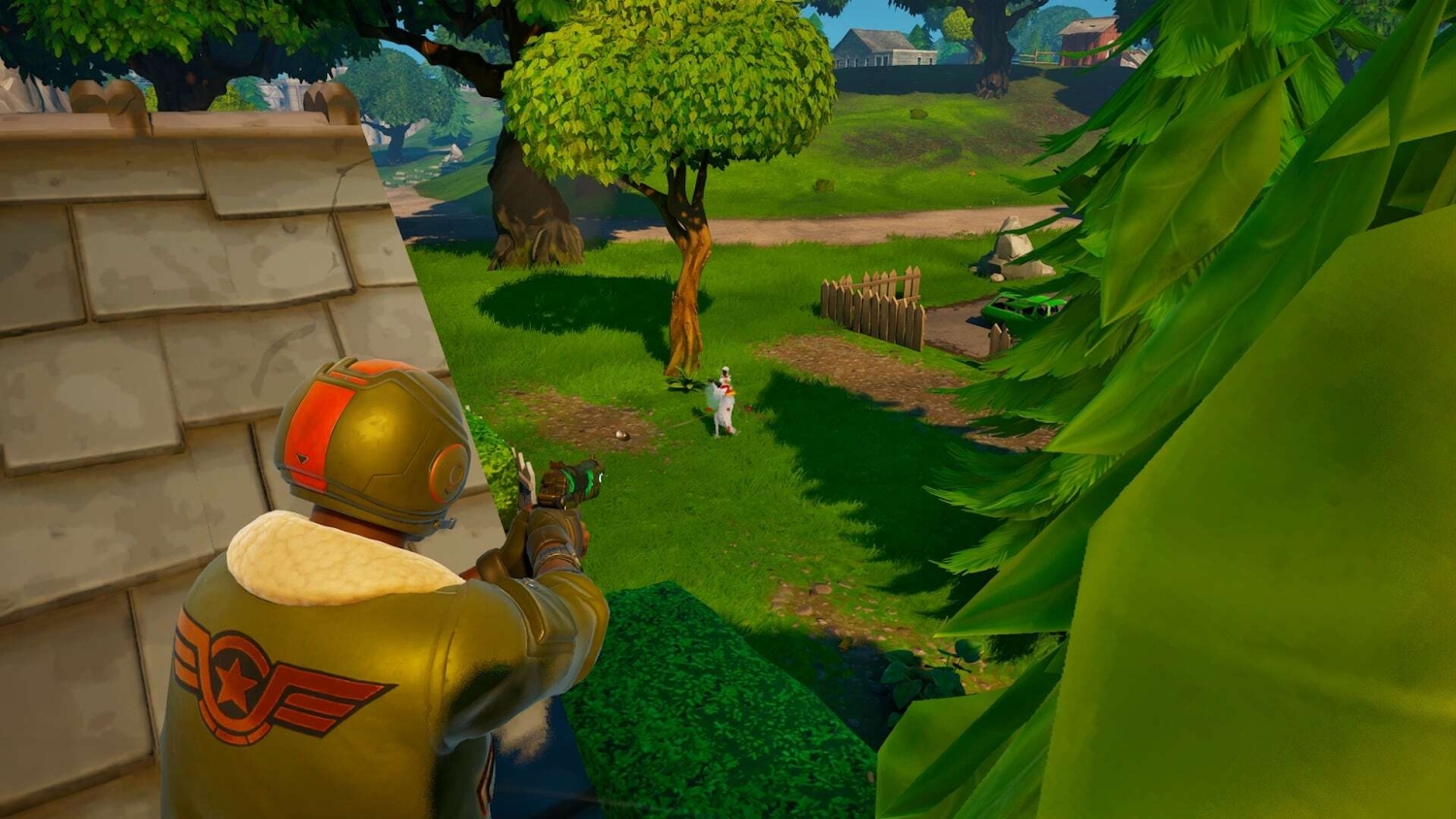 A character aims a weapon from cover on a rooftop at a llama standing near a tree in a colourful outdoor environment
