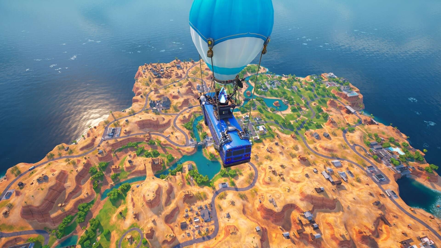 Blue and white hot air balloon carrying a vehicle over a dry island with roads and buildings near the sea