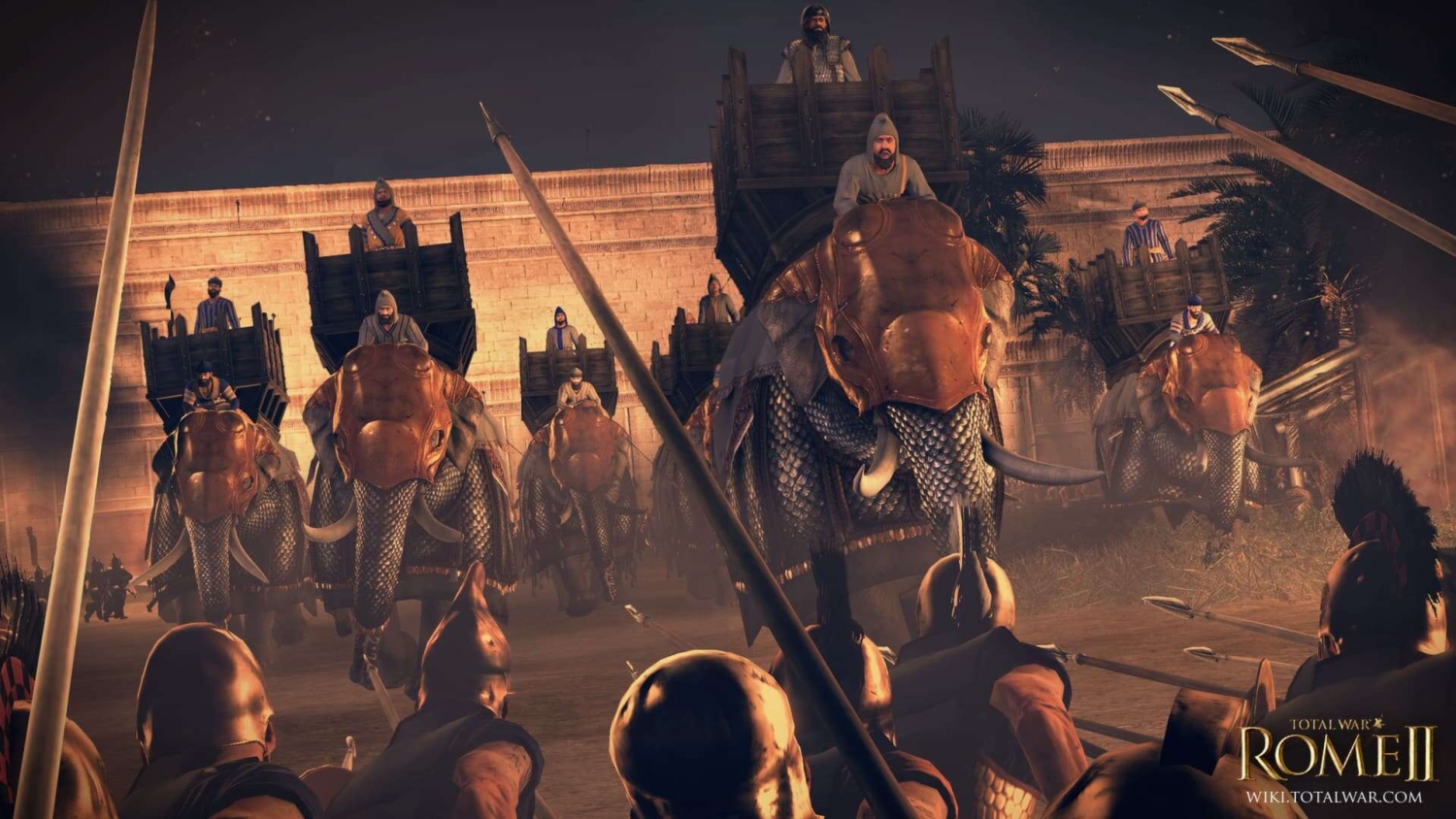 Armoured elephants with riders charging at spear-wielding soldiers in front of a large stone wall at dusk