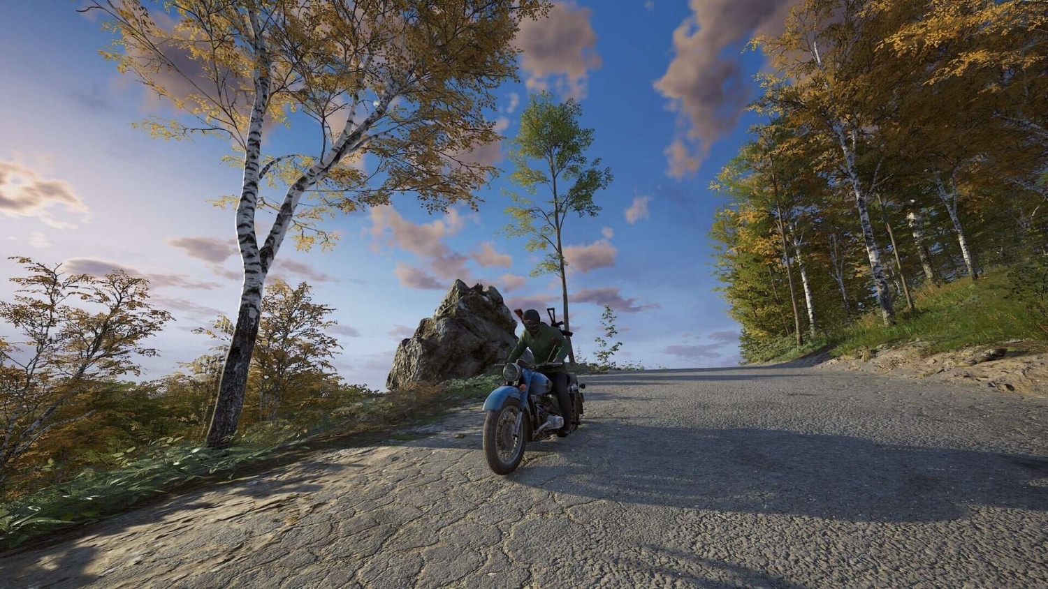 Person wearing dark clothes and helmet riding a motorcycle along a countryside road amidst autumn trees under a partly cloudy sky