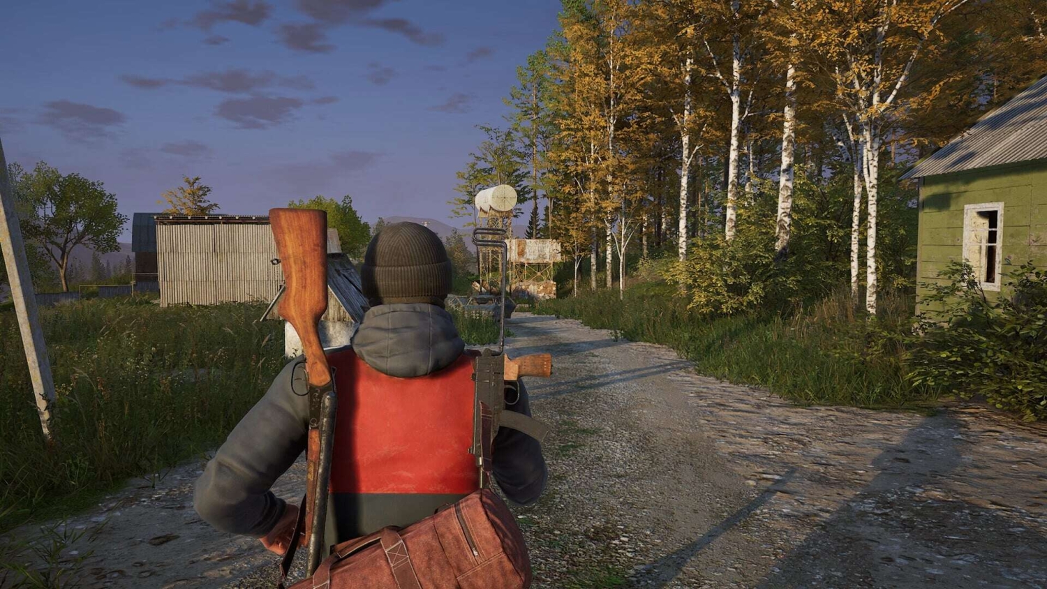 Player with backpack and rifle walking down a rural dirt path surrounded by houses and autumn trees