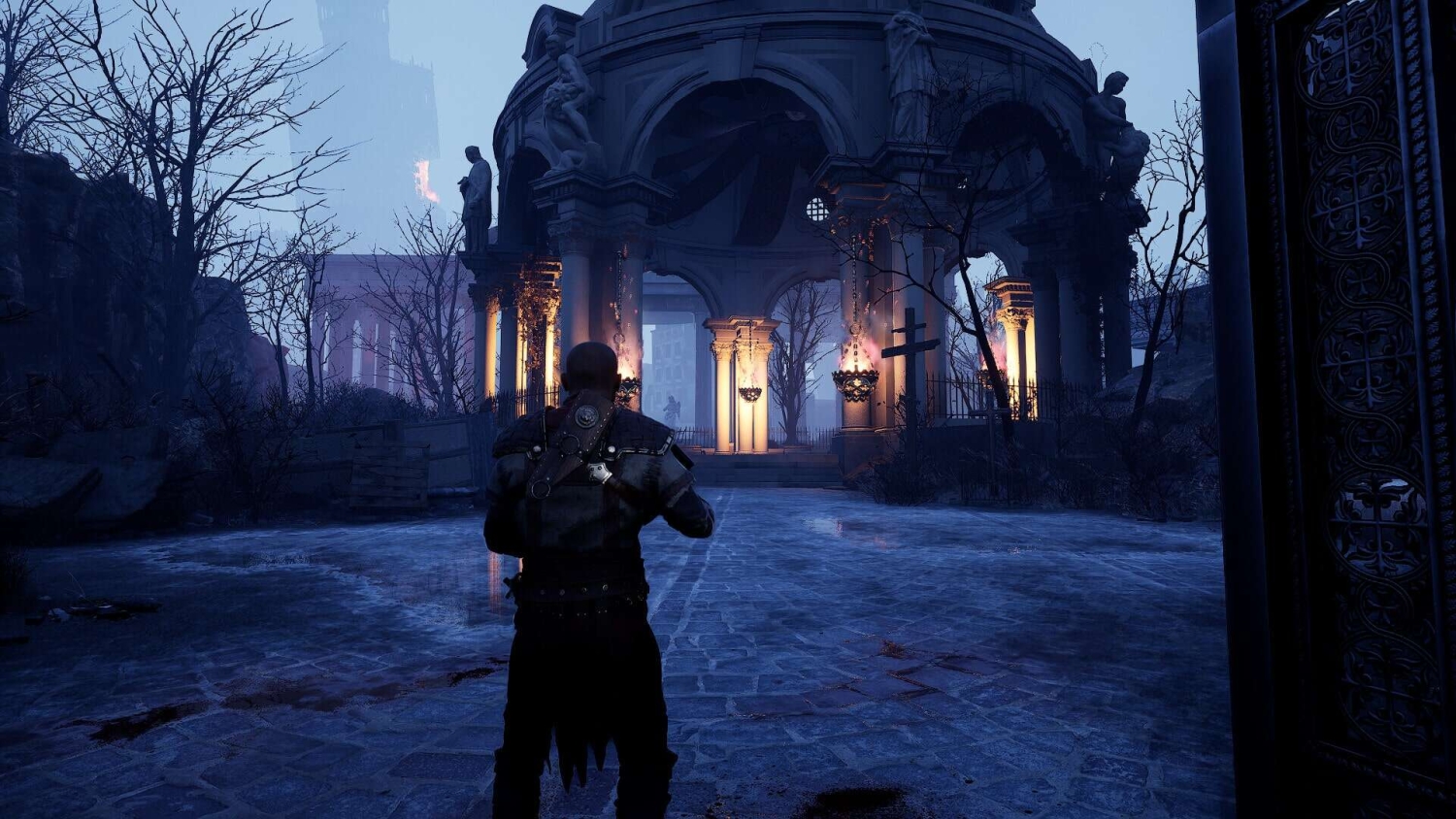 Third-person view of a character standing on wet cobblestones facing an illuminated ruin with statues and leafless trees