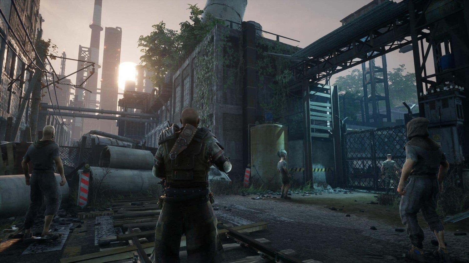 Four characters in rugged clothing stand in a overgrown industrial area with warehouses and pipes at sunset