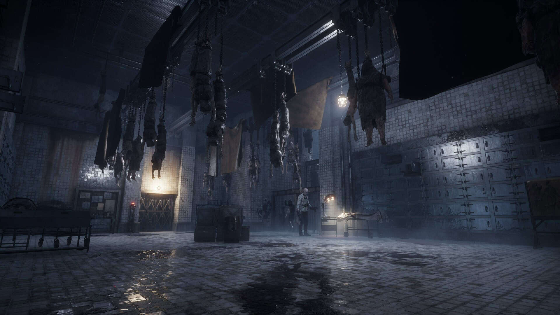 Dimly lit room with hanging bodies and a figure inspecting a table in wet tiled environment
