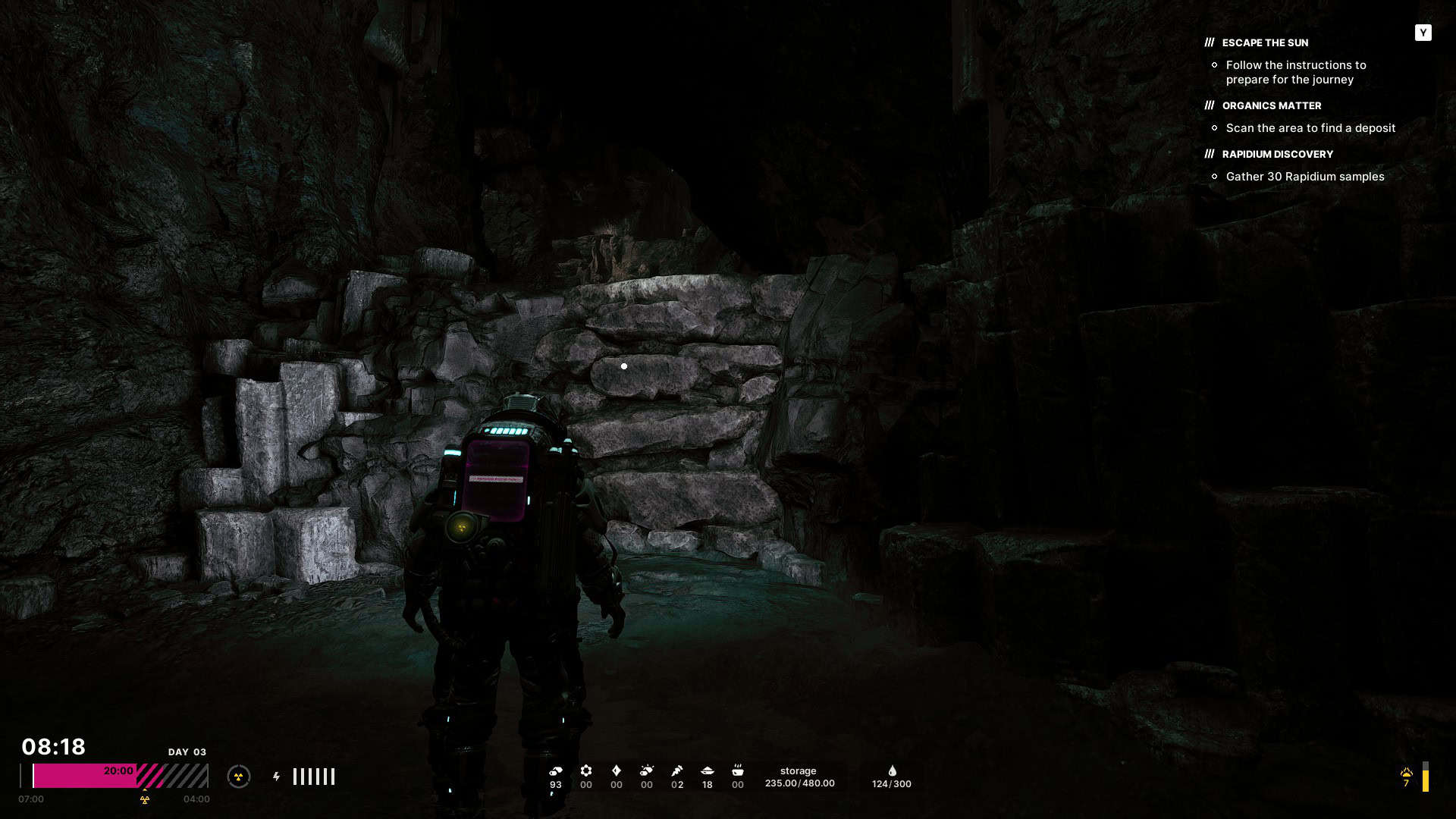 Player character in futuristic suit standing in dark cave with rocky wall ahead and mission objectives displayed on screen